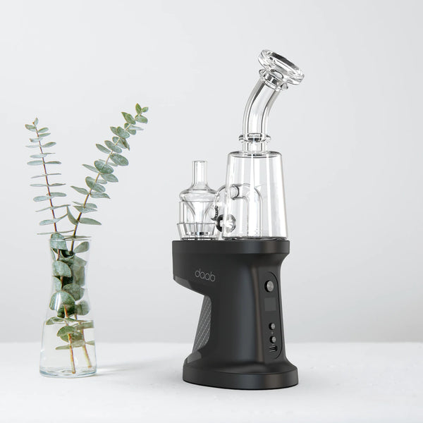 This is the daab electronic dabbing device by Ispire available at Ritual. Pictured fully assembled in front of a white background next to a plant.
